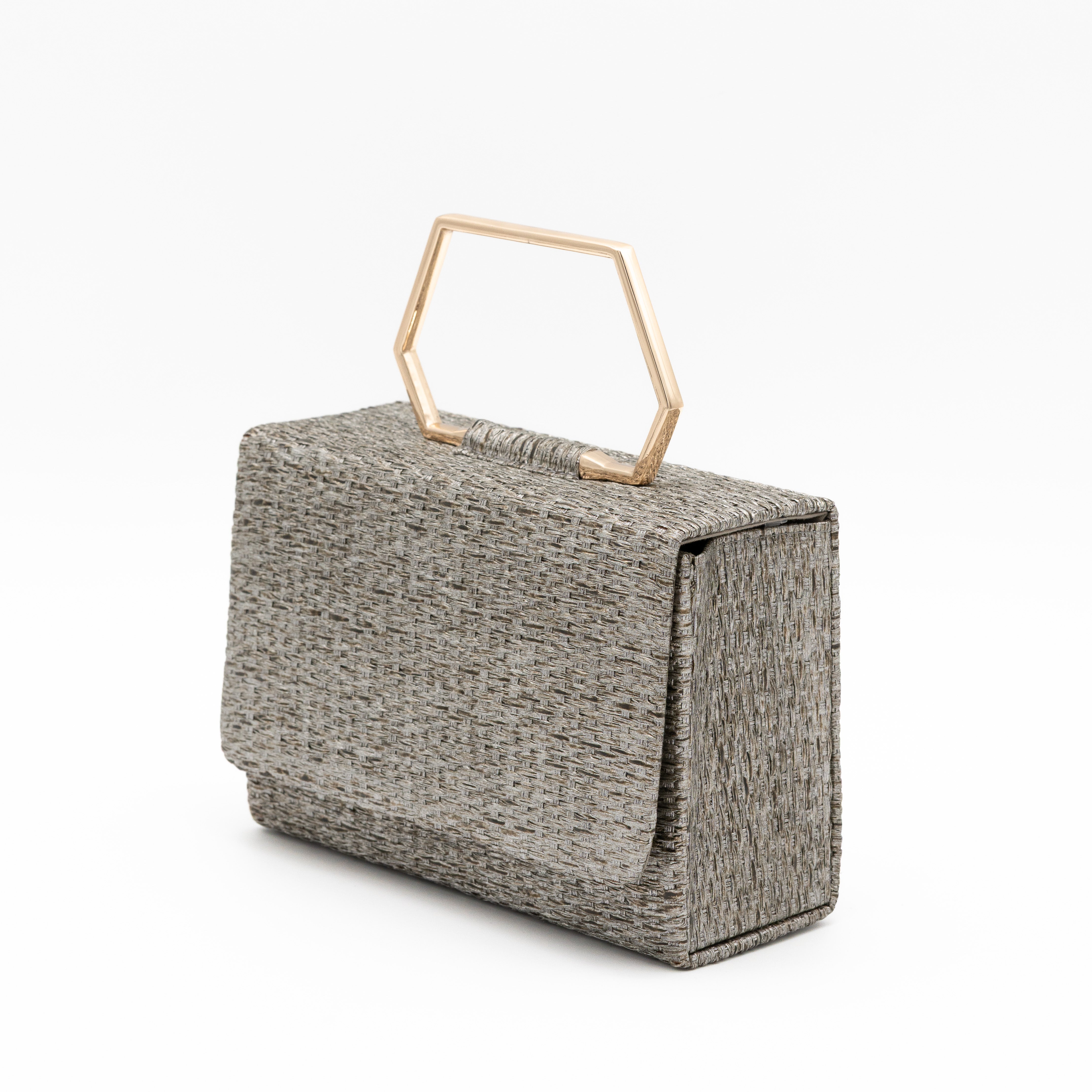 Clutch de fiesta en rafia gris con asa geométrica metálica y cierre magnético, ideal para bodas y cócteles