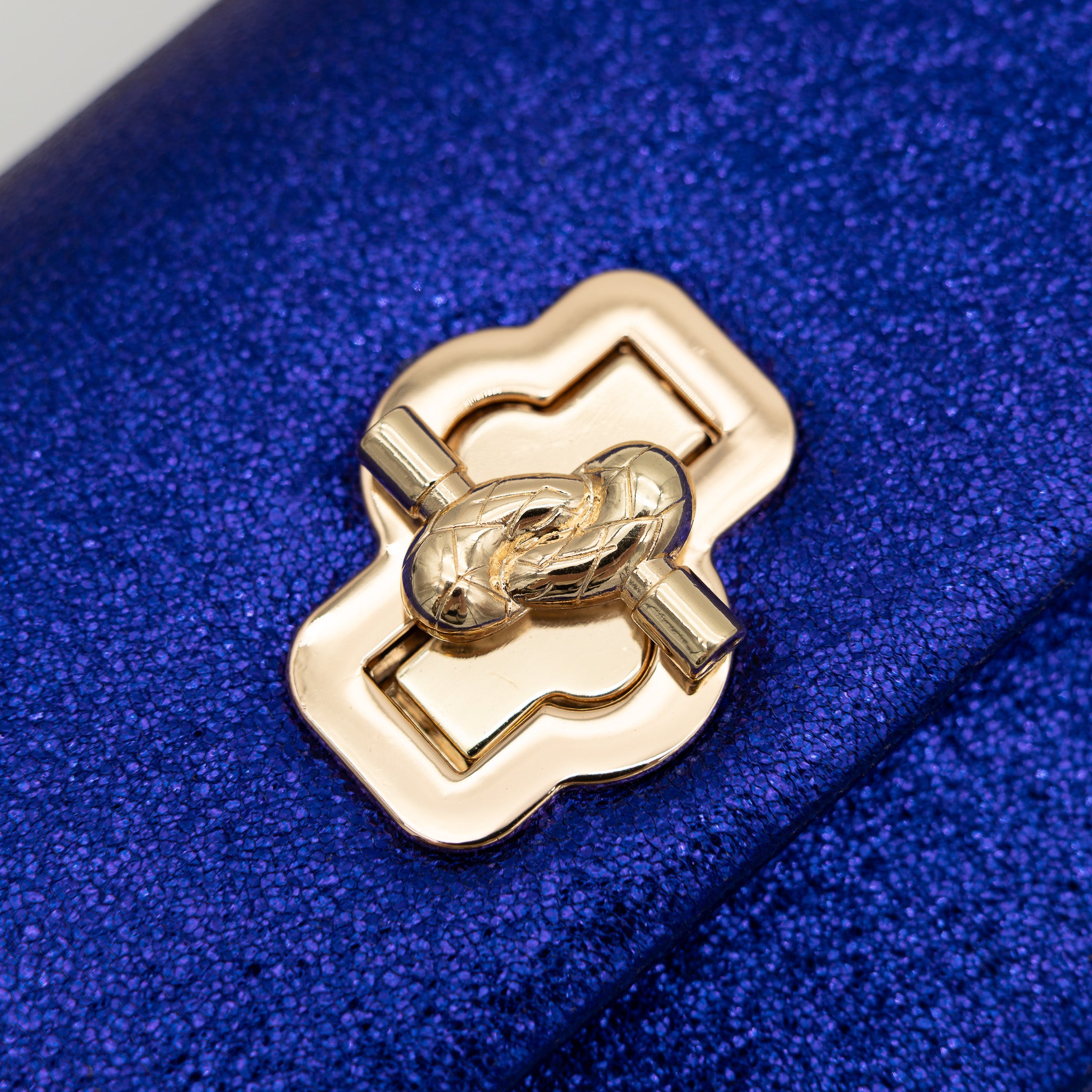 Bolso de fiesta en polipiel morado azul con acabado brillante, asa de cadena y cierre decorativo, ideal para bodas y cócteles