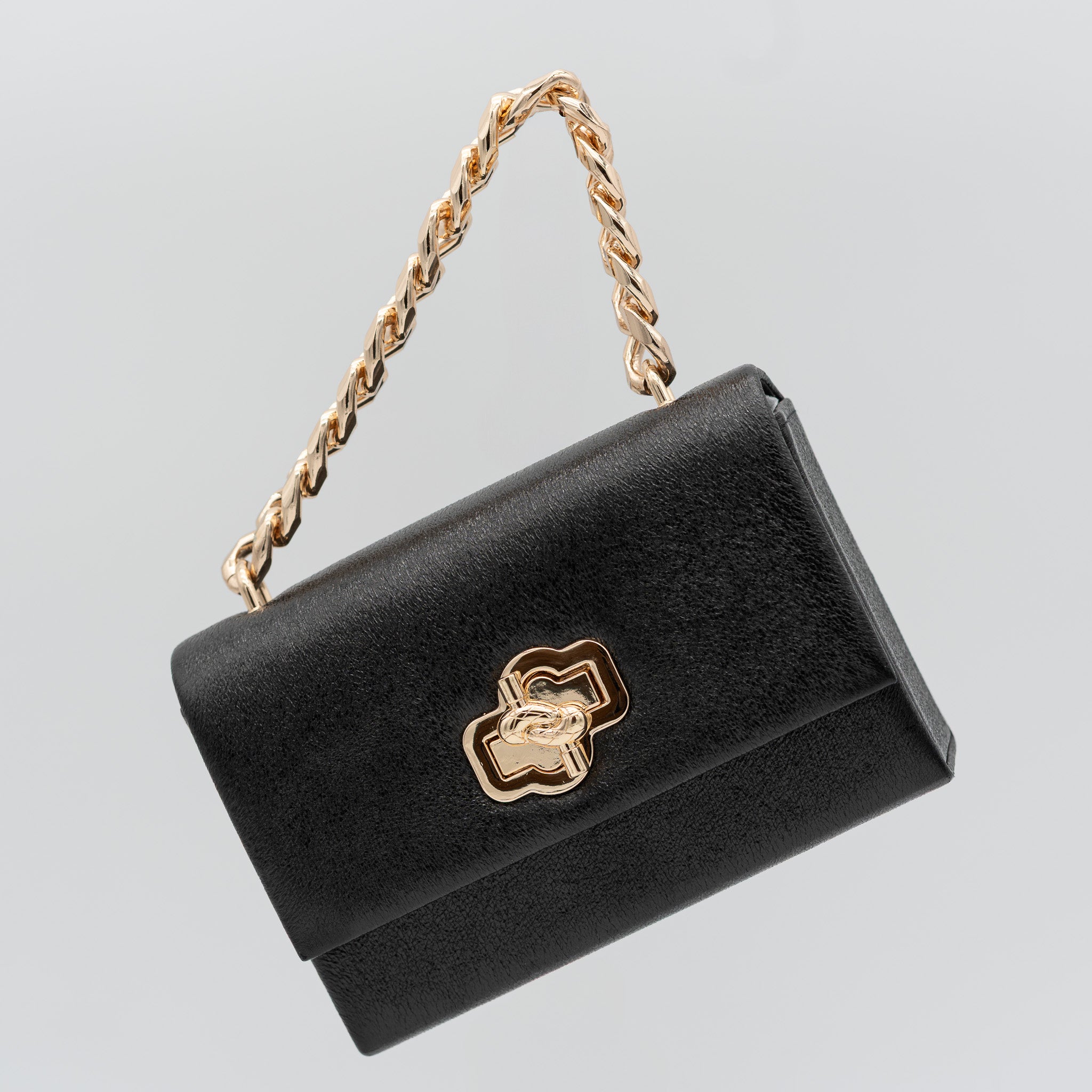 Bolso de fiesta en polipiel negro con acabado brillante, asa de cadena y cierre decorativo, ideal para bodas y cócteles