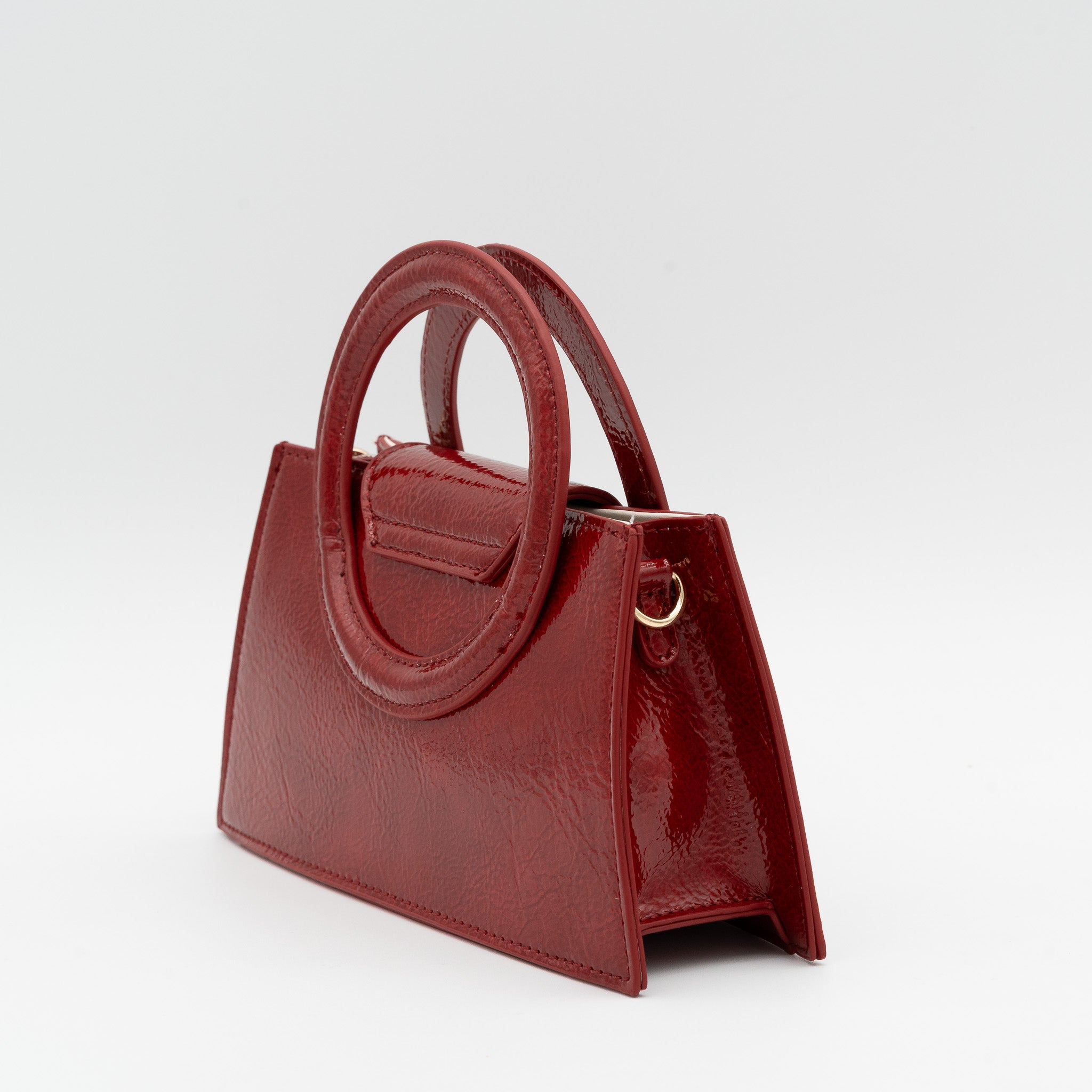 Bolso de mano rojo oscuro acharolado con asa circular rígida y cadena dorada desmontable