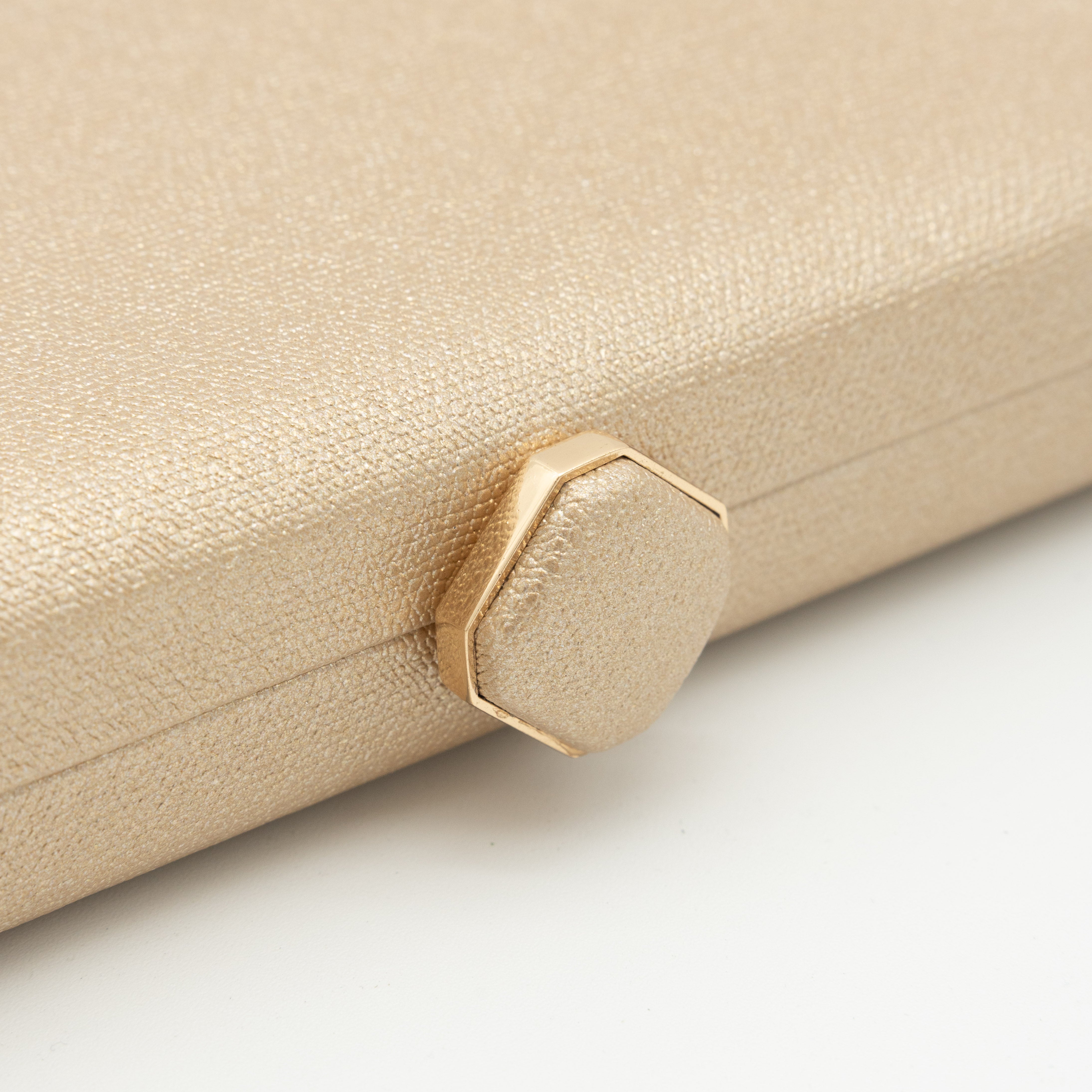 Bolso clutch de polipiel metalizado oro claro con cierre superior hexagonal y cadena desmontable